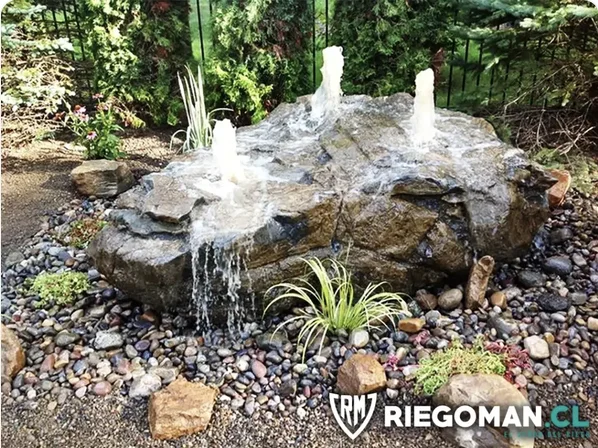 Fuente de agua tipo roca con piedras de río y surtidores en jardín